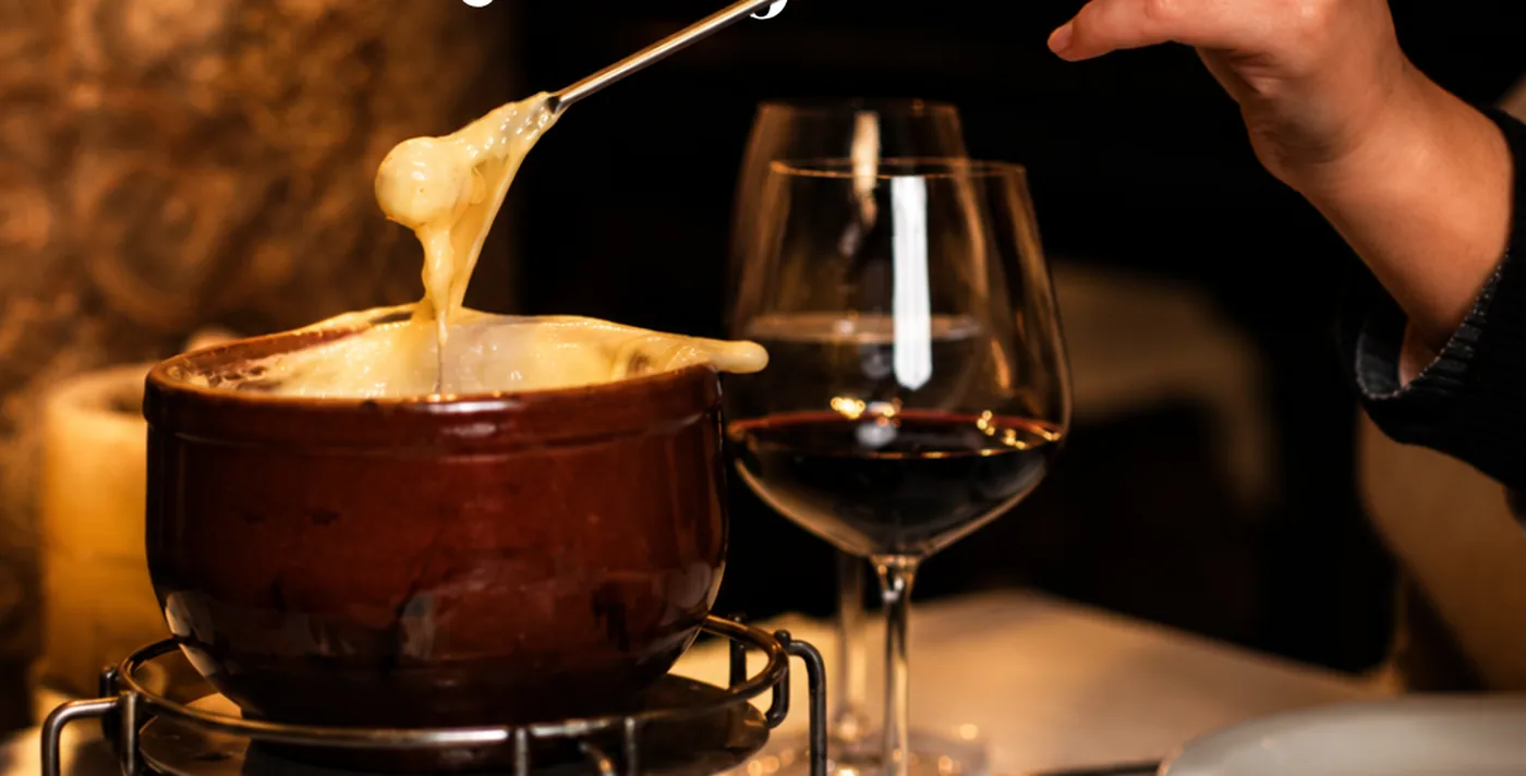 Panela de fondue de queijo ao lado de taça de vinho tinto no salão
