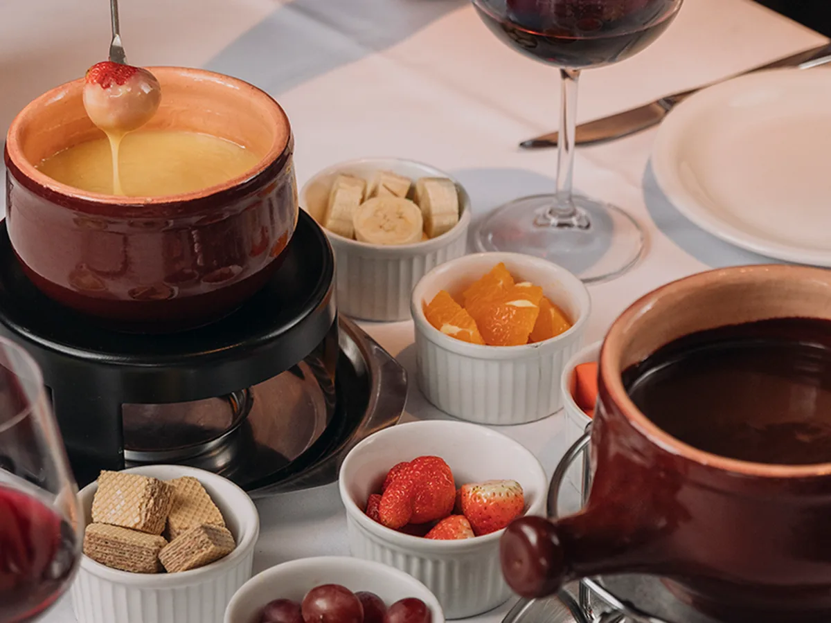 Mesa completa com fondue de queijo, chocolate e frutas
